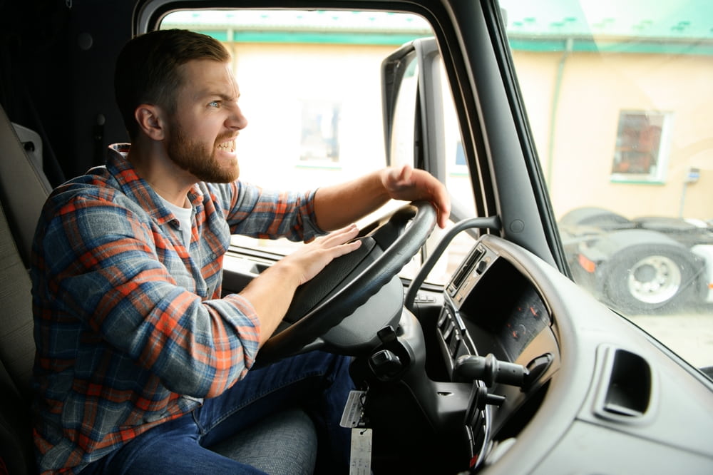 side profile of a male truck driver expressing rage and honking his horn while driving